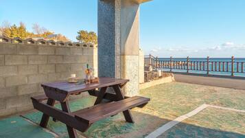 Une table de pique-nique avec une bouteille et une bougie, placée devant un paysage côtier, avec un mur de pierres et une rambarde en métal.