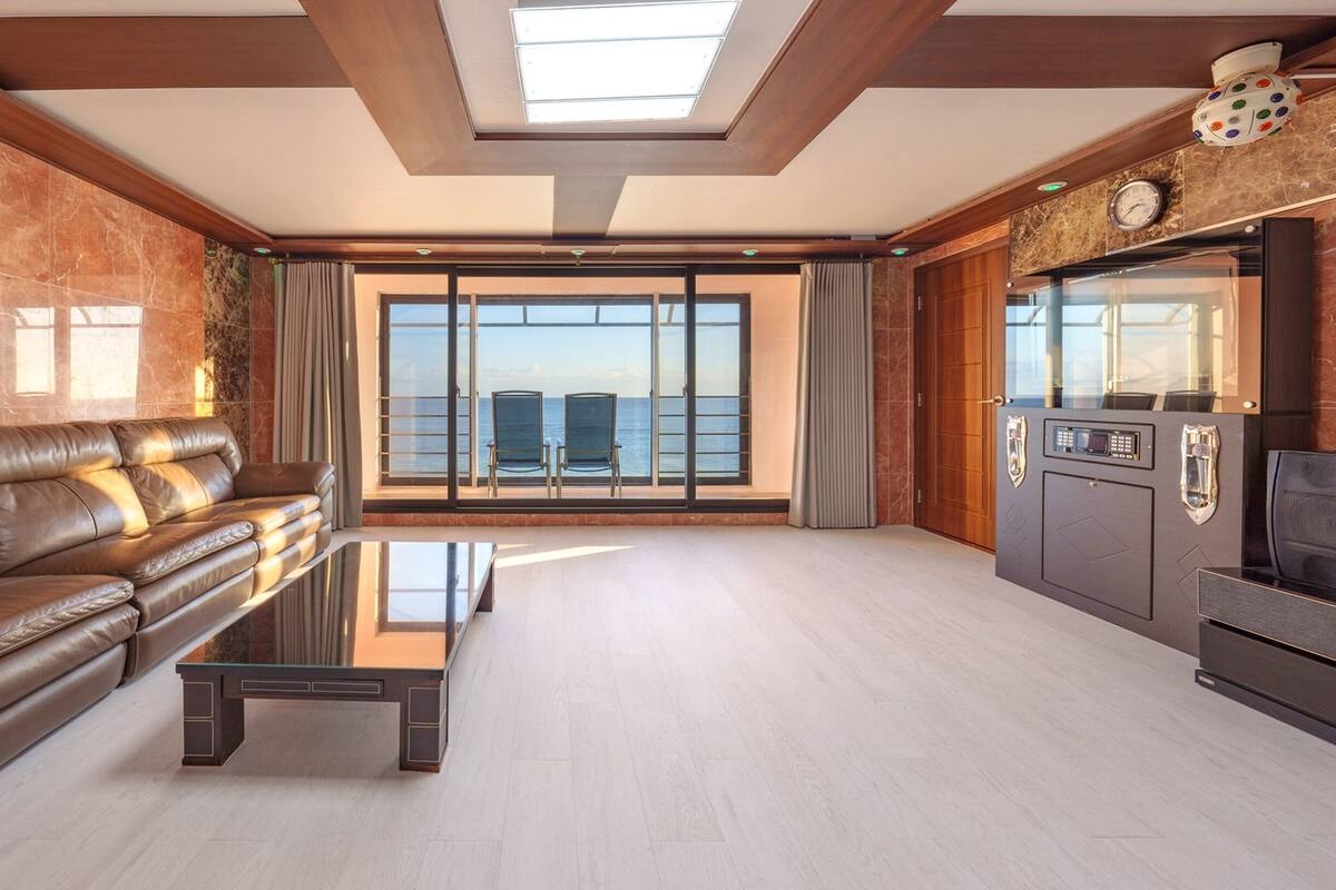 Un salon spacieux, doté d’un canapé en cuir, d’une table basse en verre et offrant une vue sur la mer grâce à de grandes fenêtres.