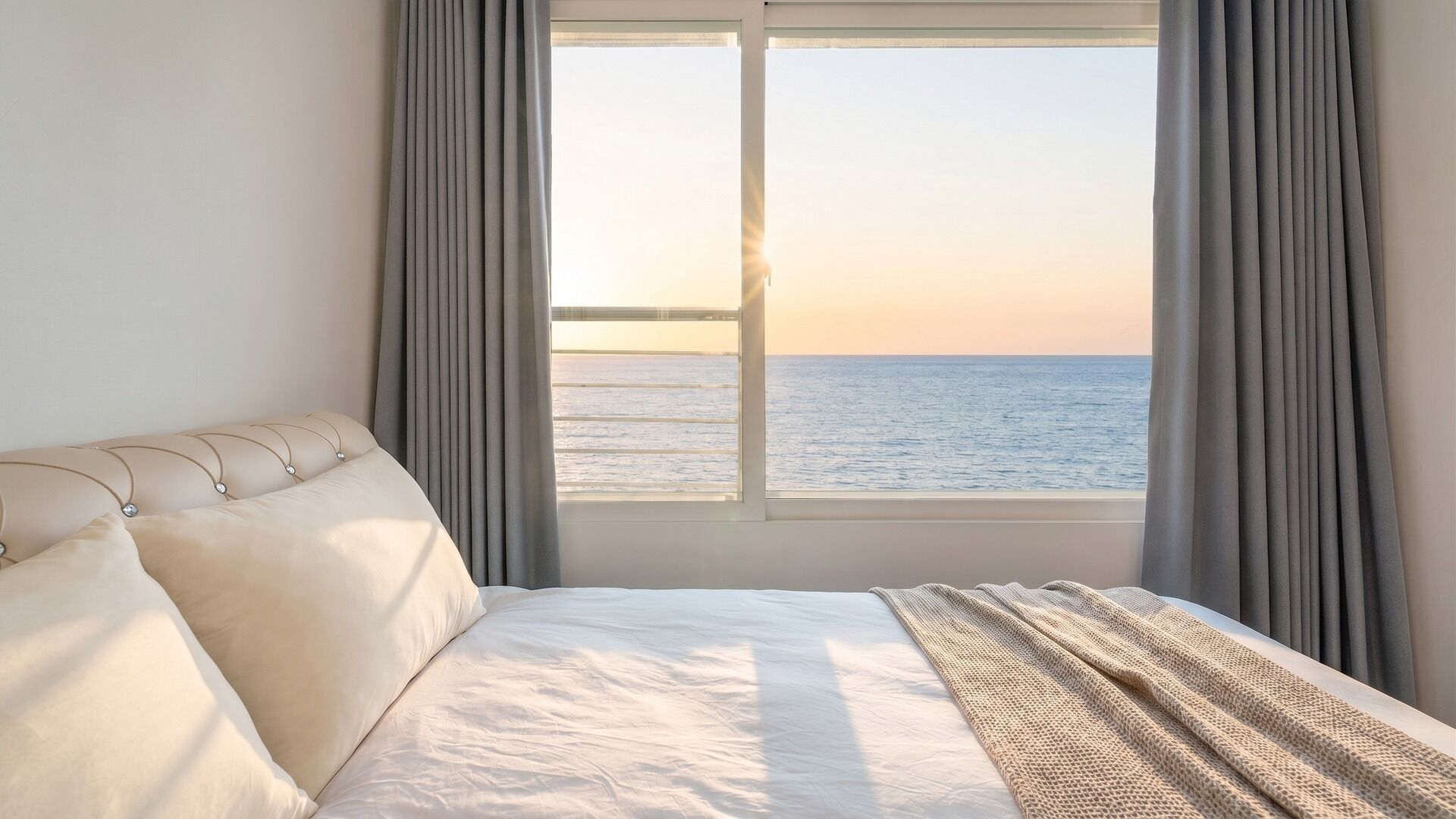 Un dormitorio con cama, vista al mar a través de una ventana y cortinas.