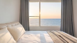 Une chambre à coucher avec un lit, une vue sur la mer par la fenêtre et des rideaux.