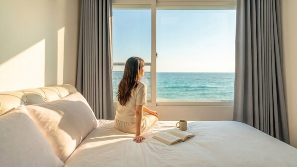 A room with a bed, a window with curtains, and a view of the sea.