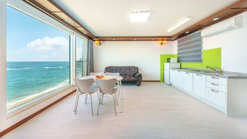 A modern kitchen with a view of the ocean, a dining area with chairs, and a sofa.