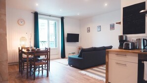 A modern living room with a dark sofa, wooden dining table, and chairs. A flat-screen TV is mounted on the wall, and a chalkboard menu is visible. - Pop Art, Centre de Tours (Tours)