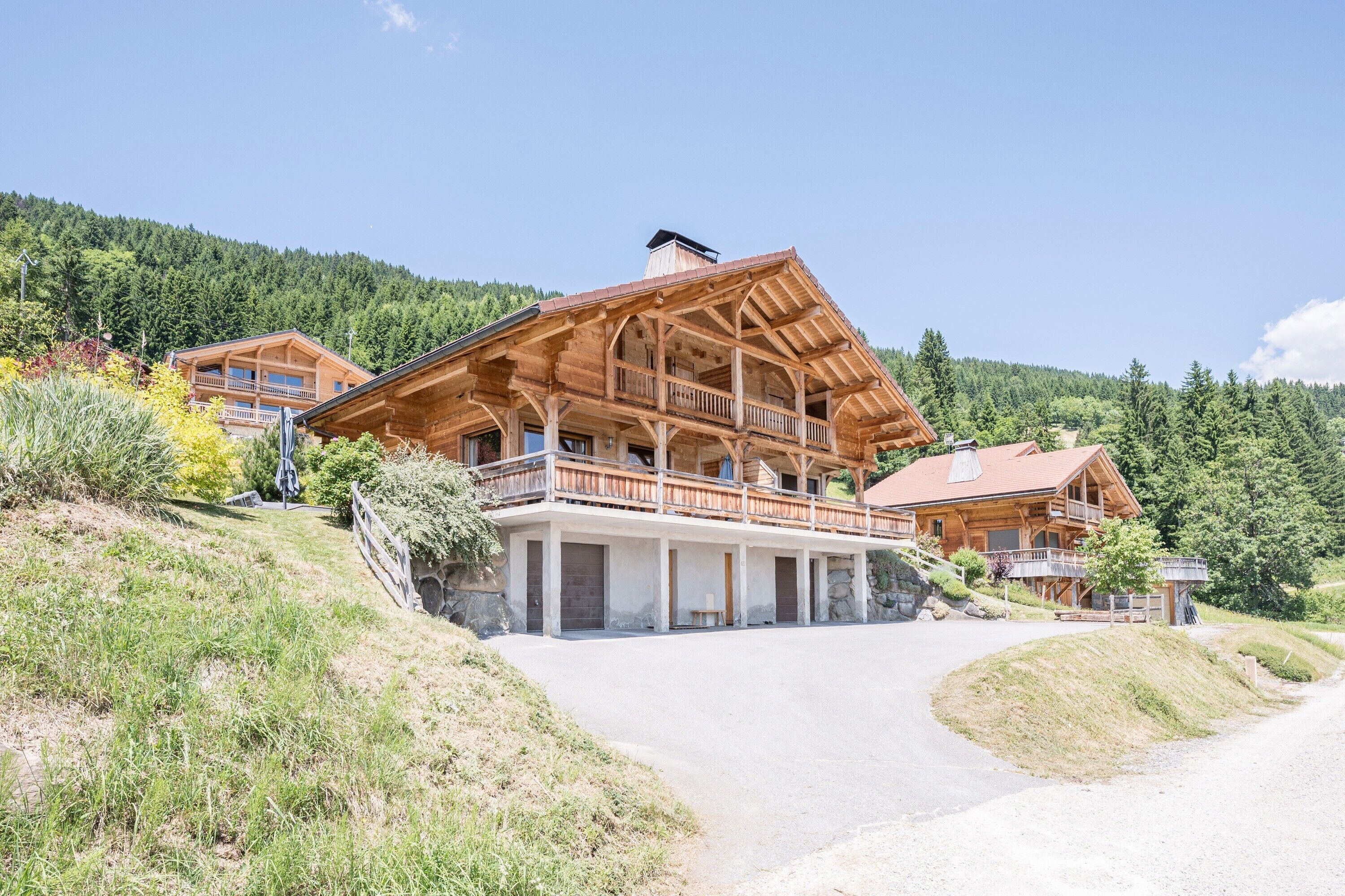 Un grand chalet en bois doté de nombreux balcons et fondé sur des pierres, situé au milieu d’une colline boisée.