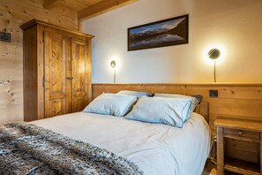 A wooden cabin-style bedroom with a bed, a large wardrobe, a framed picture on the wall, and two wall-mounted lights. - Chalet 'Bernard' with Mountain View, Private Terrace and Wi-Fi (Manigod)
