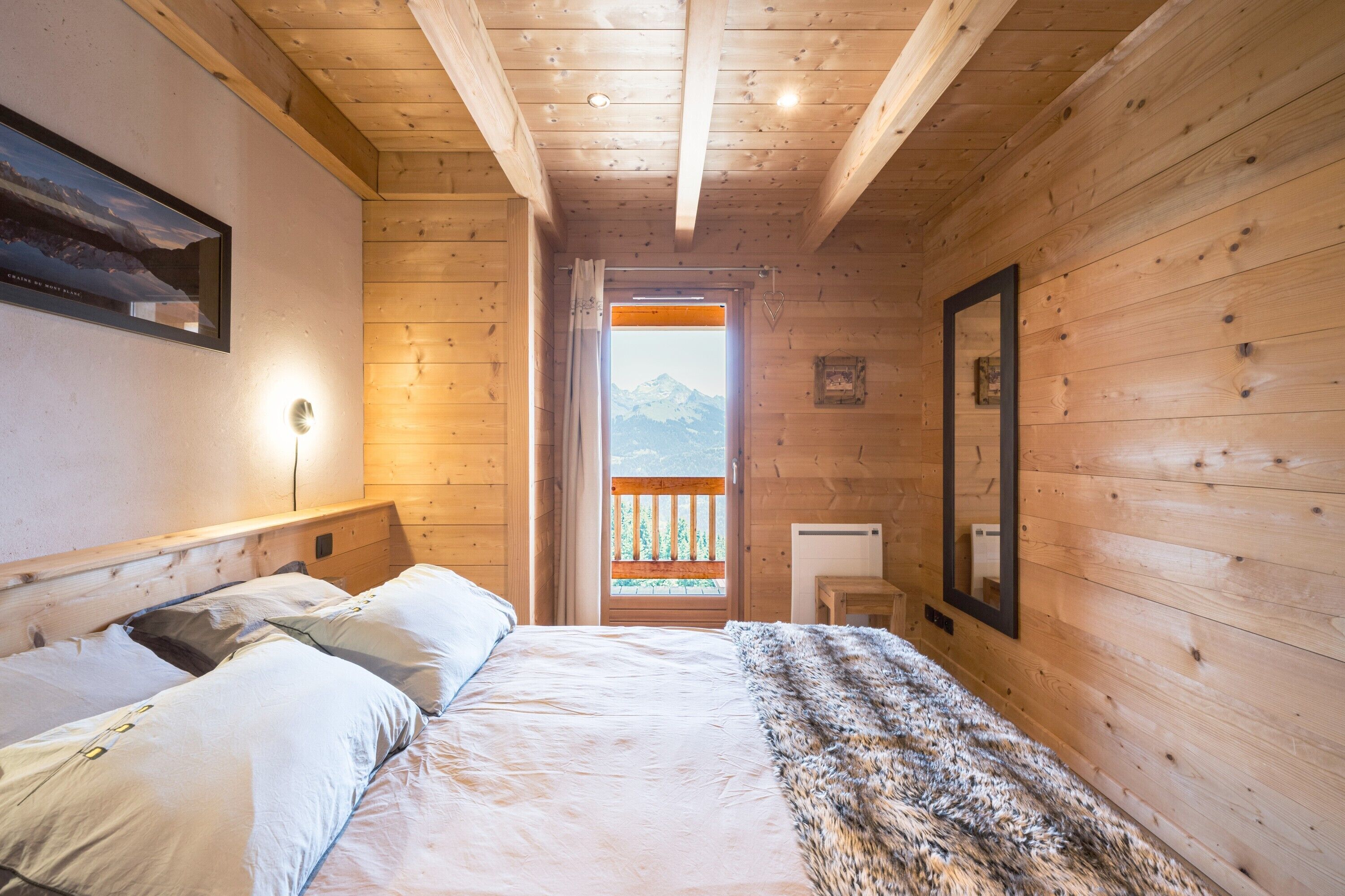 Un dormitorio de cabaña de madera con una cama, un espejo y una ventana con vista a la montaña.