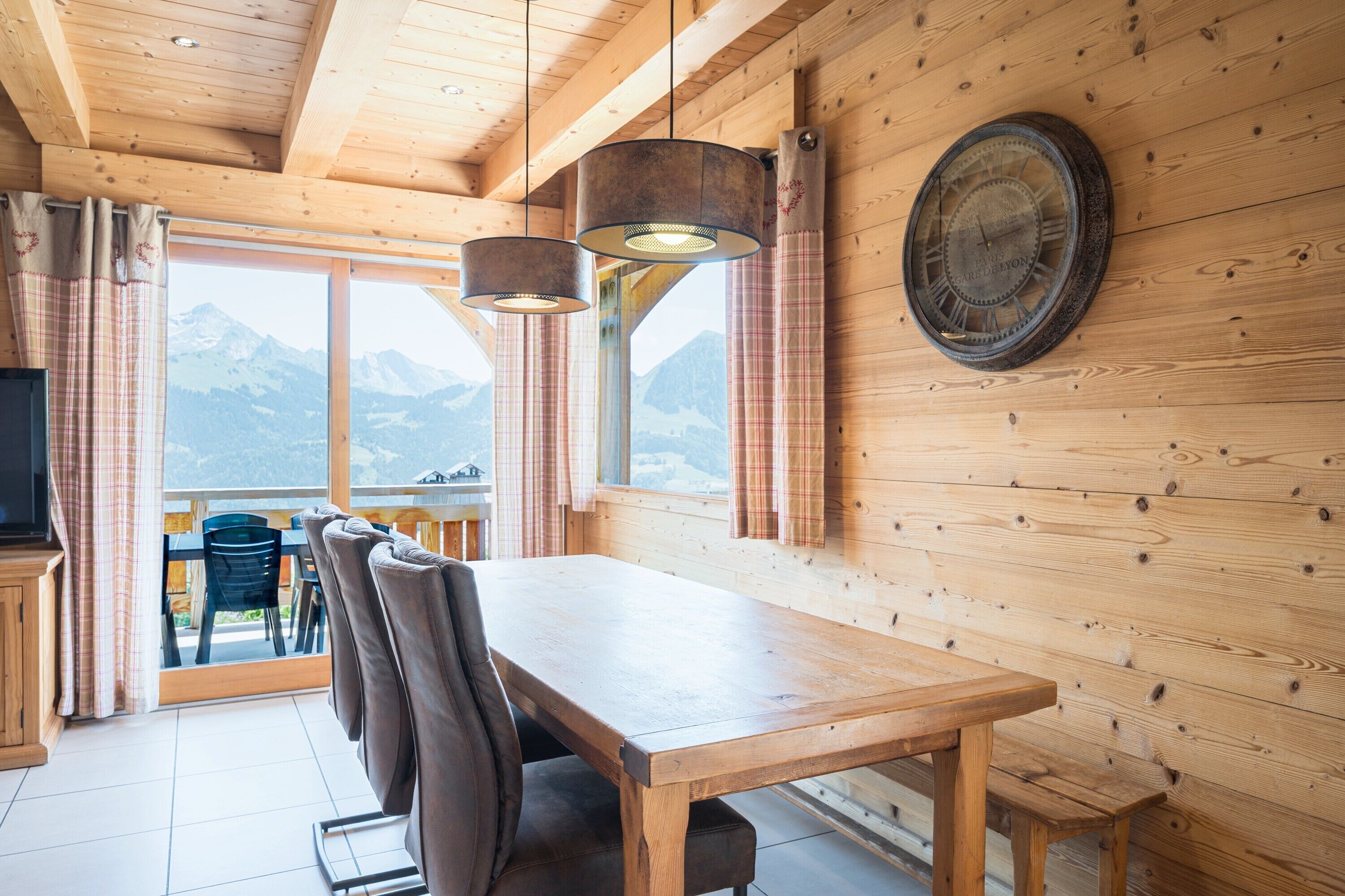 Un interior de madera con una mesa de comedor, sillas y un ventanal con cortinas.