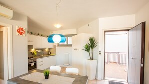 Une cuisine moderne avec des meubles blancs, une table à manger avec des chaises, une plante en pot et une vue sur le balcon.