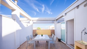 Une terrasse couverte avec une table et des chaises, un évier et une vue sur la ville.