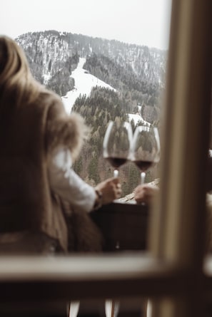 Une personne tenant un verre de vin, avec en arrière-plan, à travers une fenêtre, un paysage de montagne enneigé.