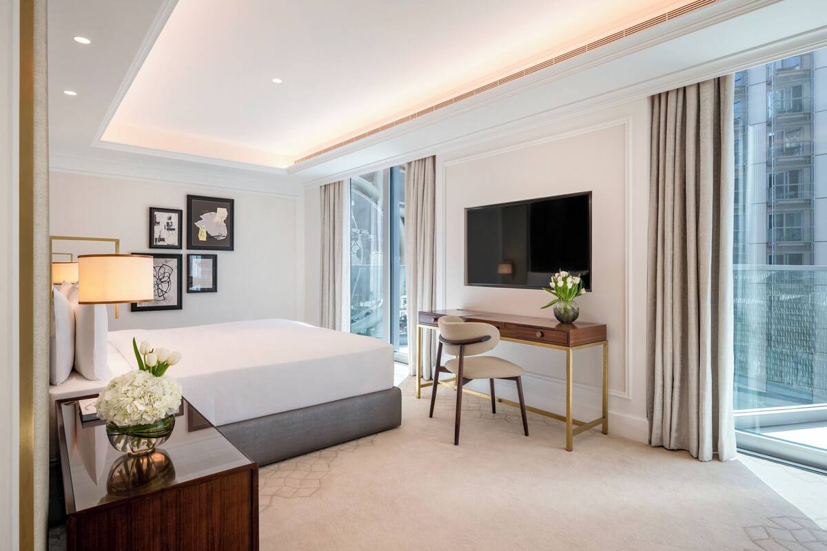 A modern hotel room with a large bed, a desk, a TV, and a view of the city.