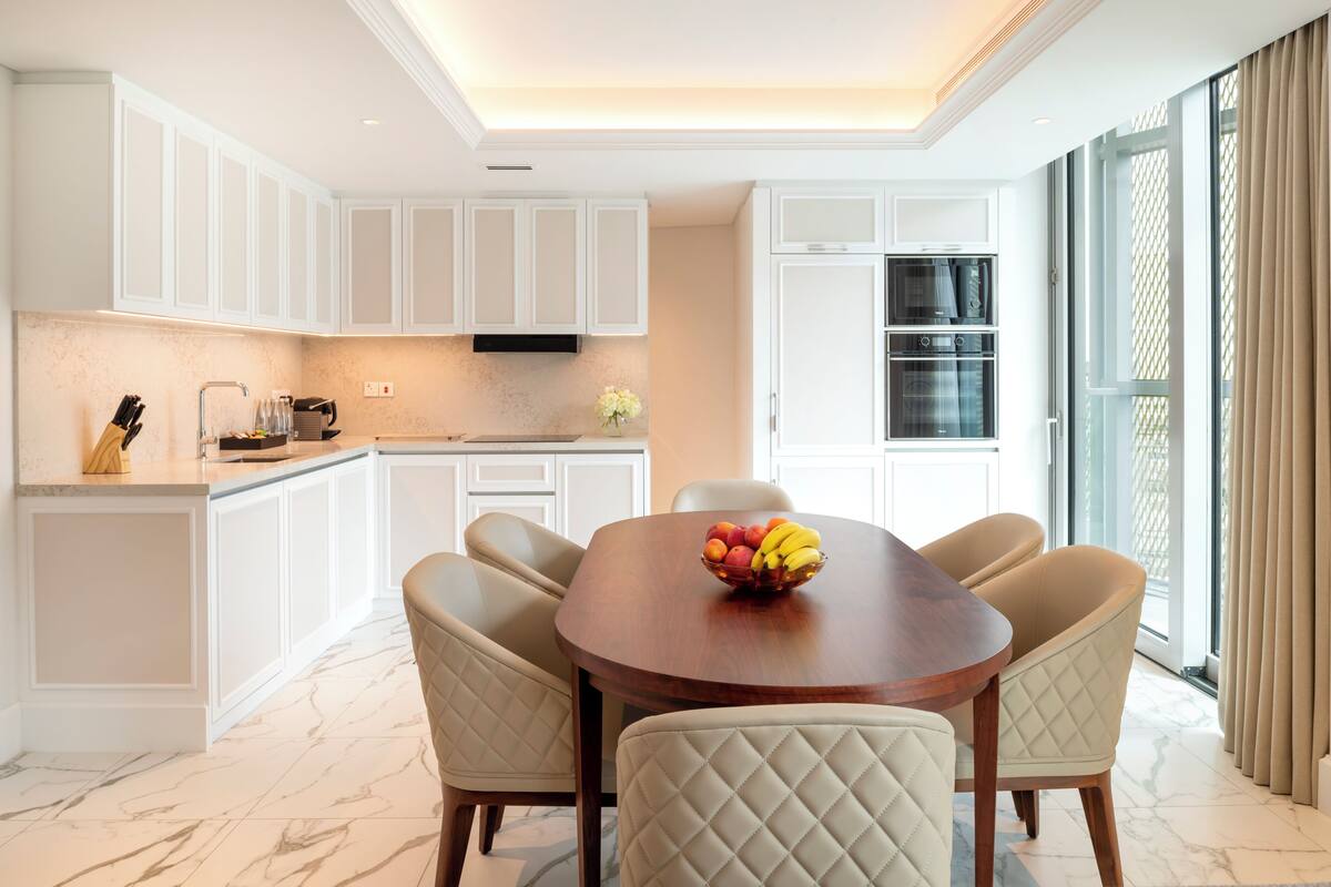 A modern kitchen with white cabinetry, a dining table with six chairs, and a fruit bowl on the table.
