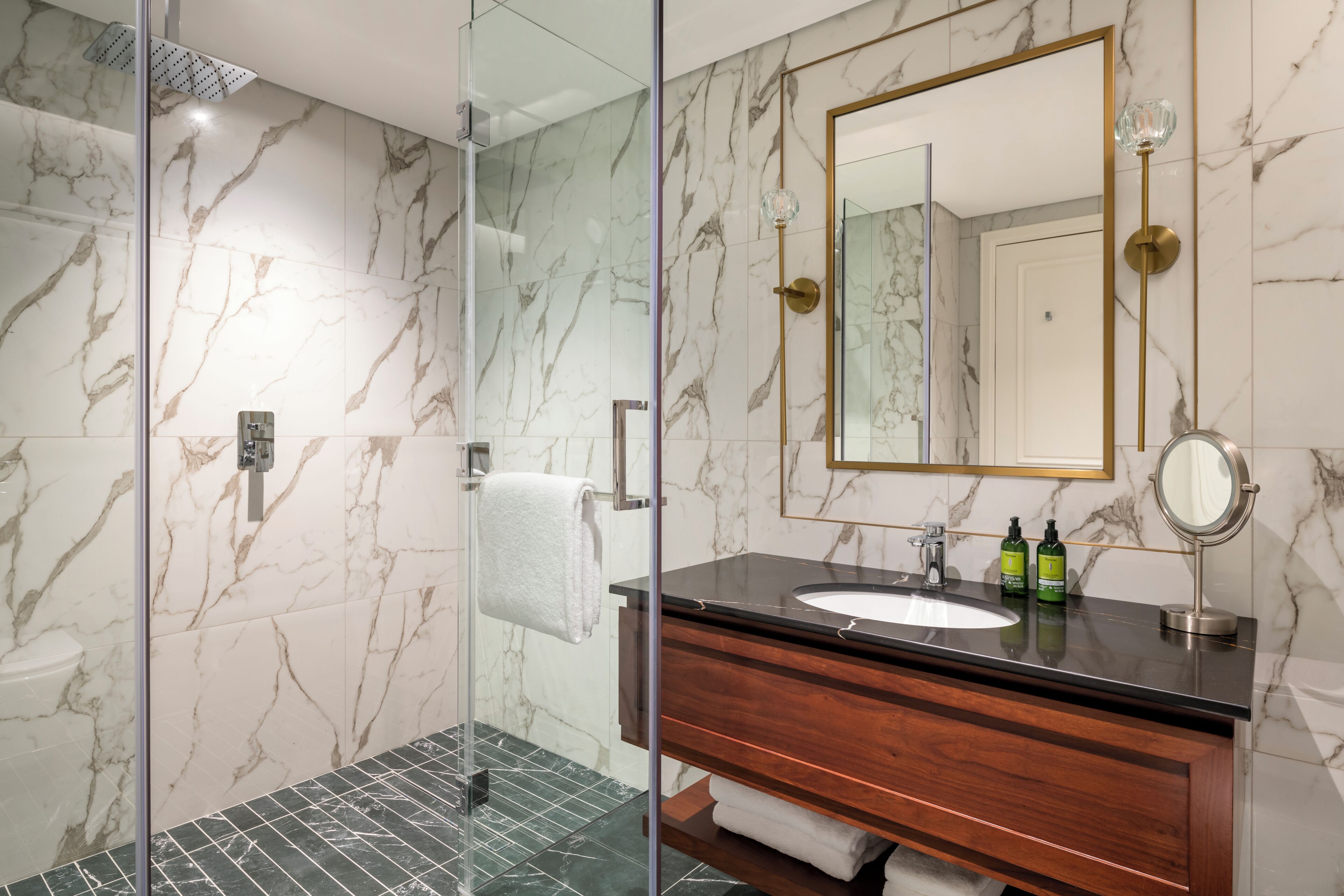 A modern bathroom with a glass shower enclosure, marble walls, a wooden vanity, and a large mirror.