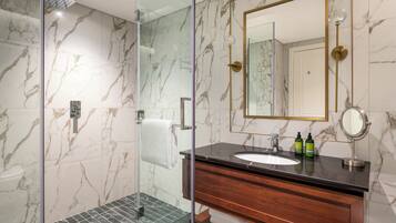 A modern bathroom with a glass shower enclosure, marble walls, a wooden vanity, and a large mirror.