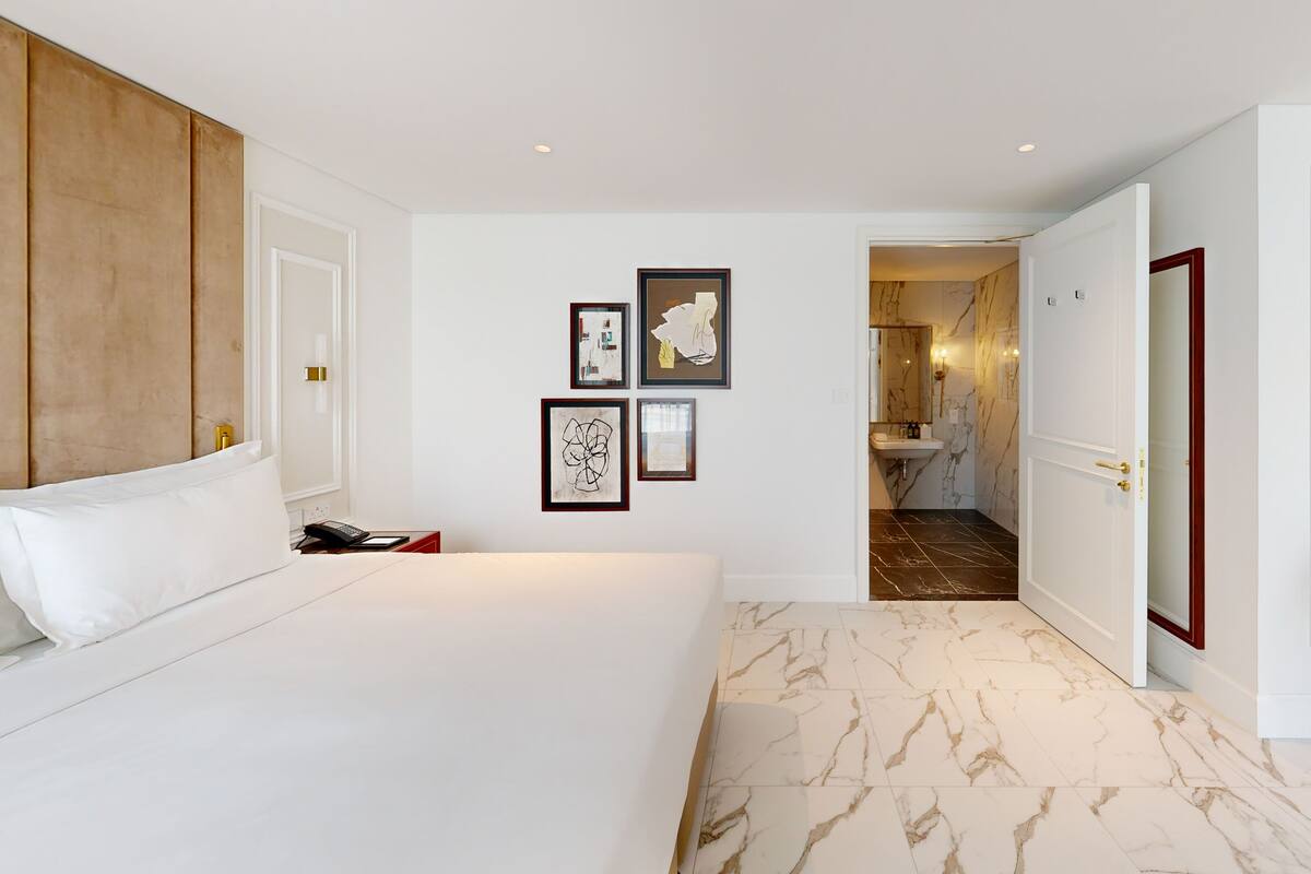 A hotel room with a large bed, a wooden headboard, a small desk with a chair, and a bathroom visible through an open door.