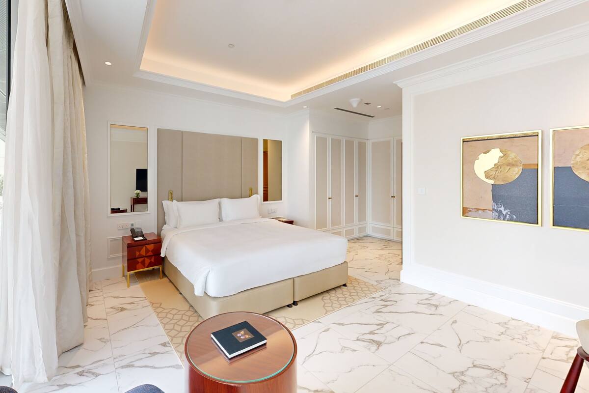 A hotel room with a large bed, a bedside table, a round coffee table, and a large mirror.