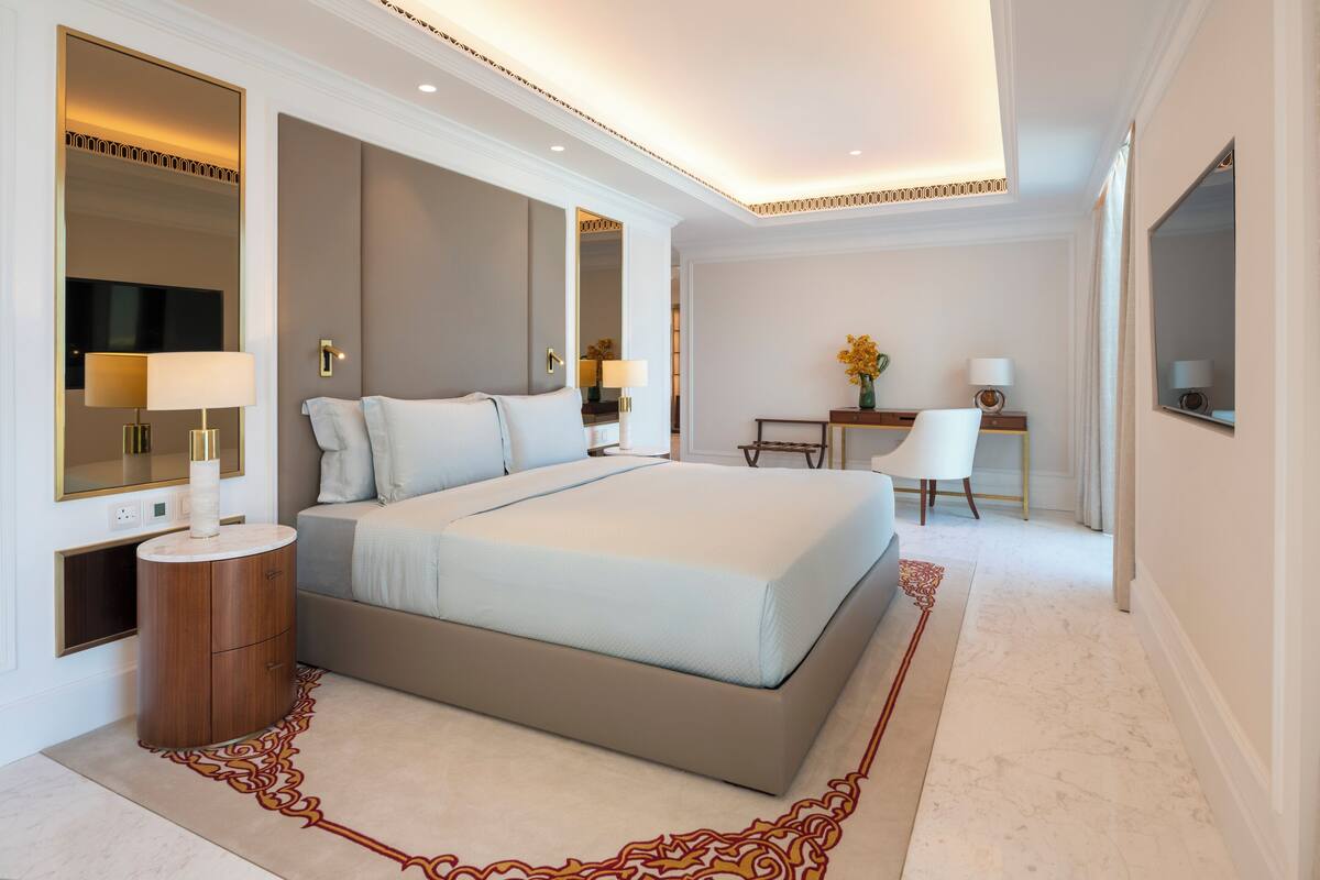 A modern hotel room with a large bed, bedside tables, a desk, and a chair.