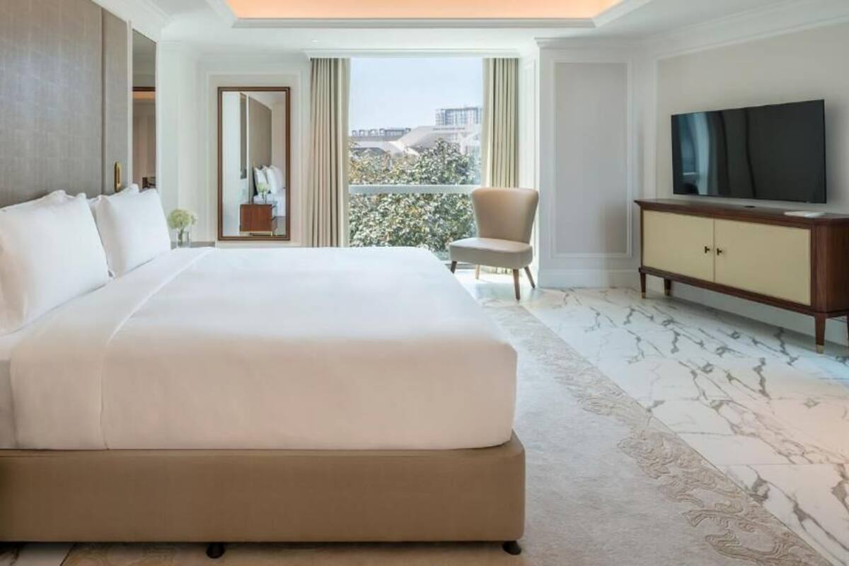 A hotel room with a large bed, a TV, a chair, and a balcony with a view.