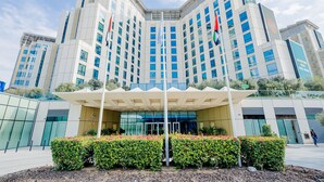 A modern hotel with a symmetrical facade, multiple flags, and a central entrance with a canopy. - Cheval Maison Expo City Dubai (Dubai)