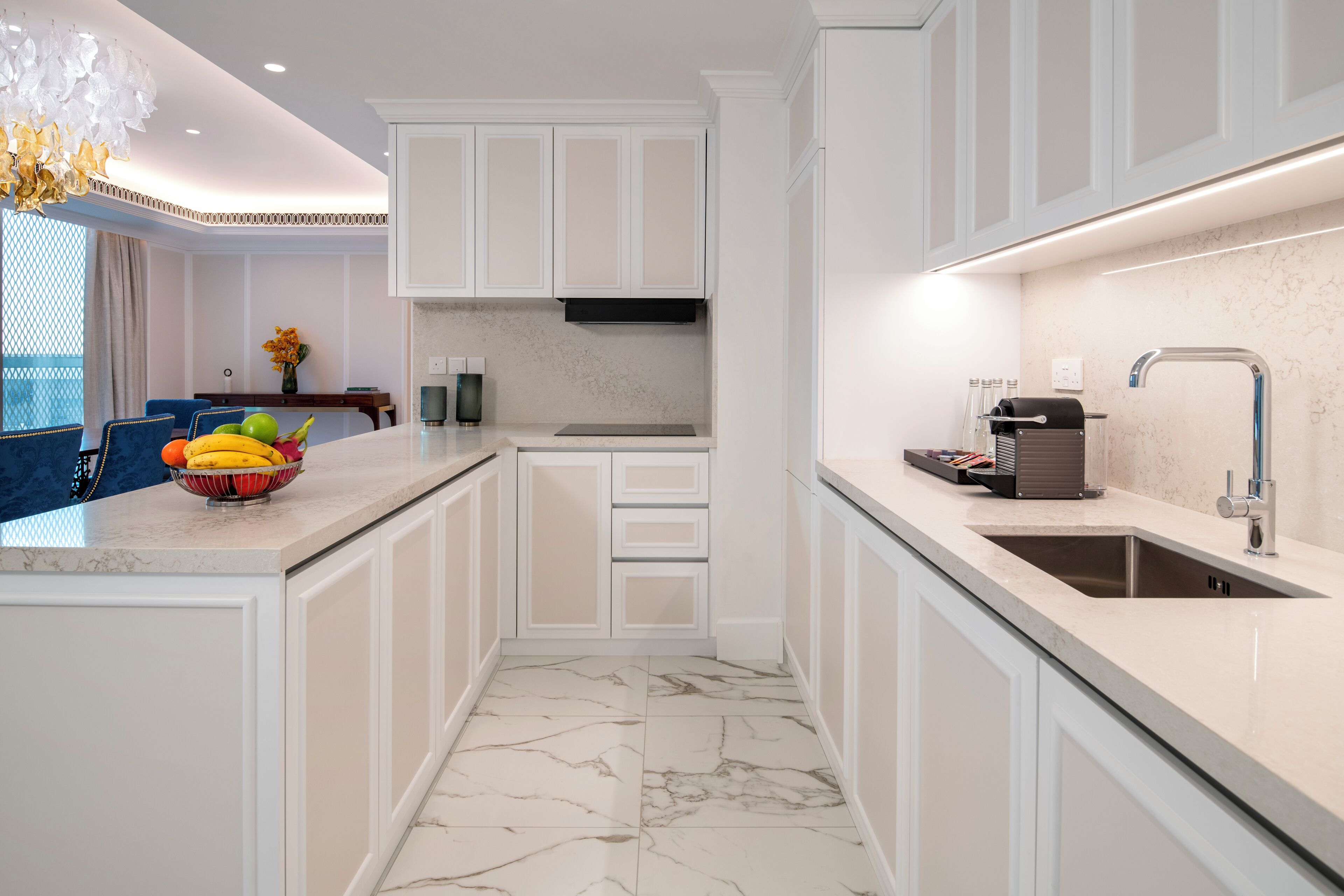 Una cocina moderna con armarios blancos, piso de mármol y una isla integrada con frutero.