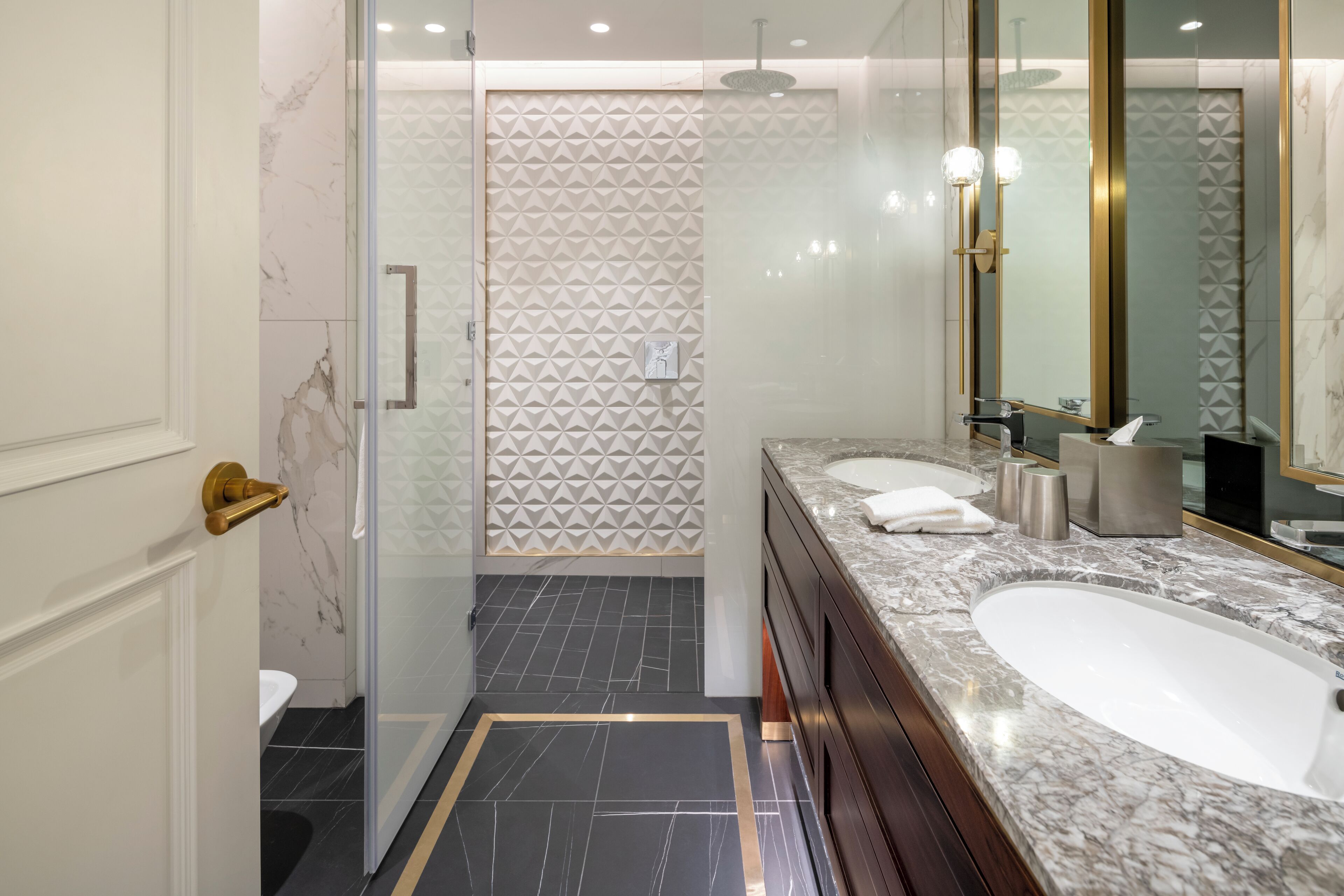 A modern bathroom with a large sink, a glass shower enclosure, and a marble floor.