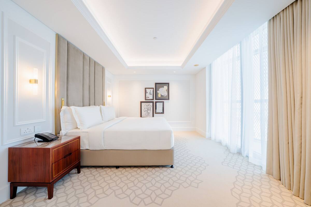 A hotel room with a bed, bedside table, wall-mounted light, and framed artwork.