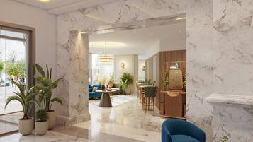 Un moderno vestíbulo de hotel con suelo de mármol, un sillón azul y una zona de comedor con mobiliario de madera.