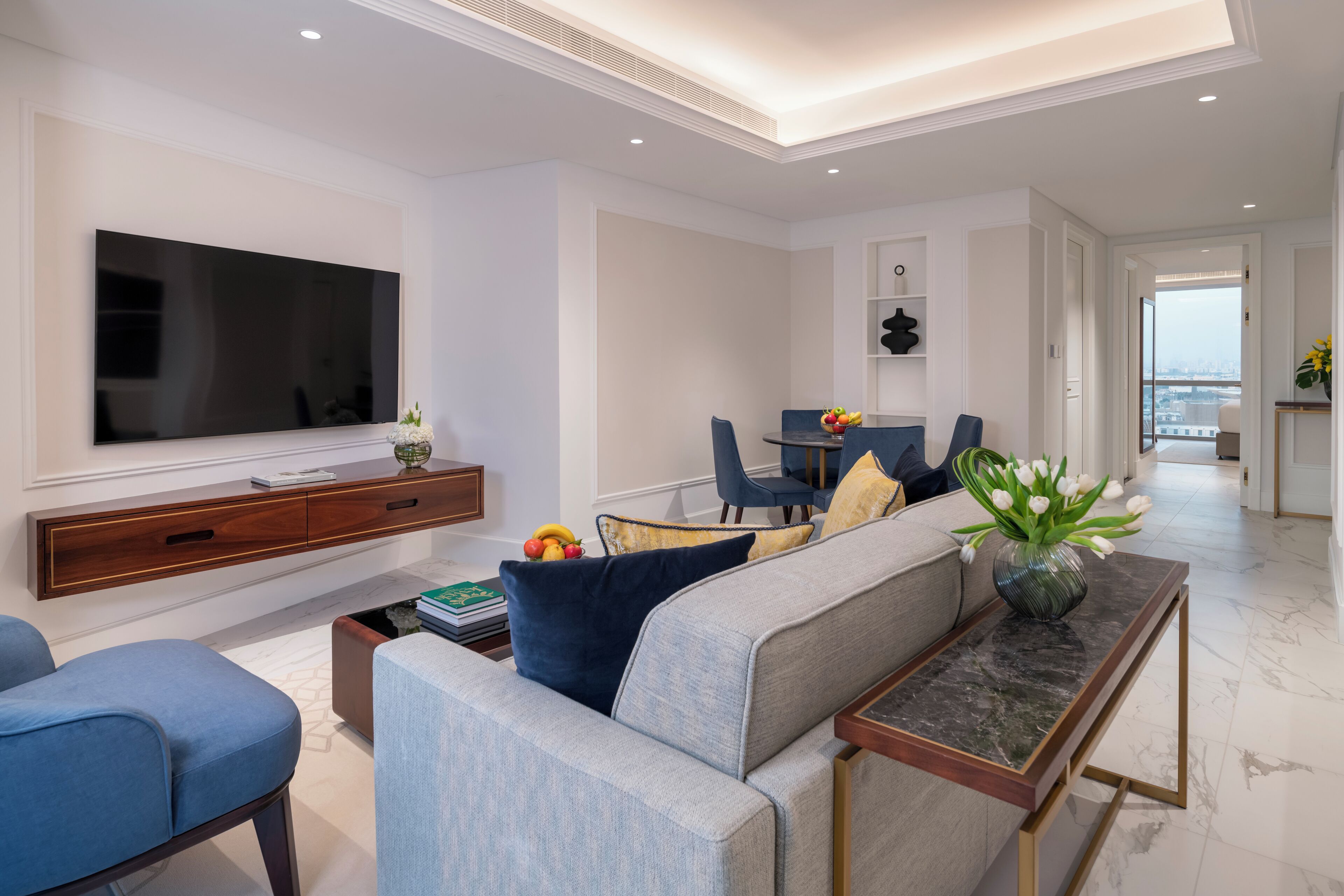 A modern living room with a large flat-screen TV, a sofa, and a dining area with chairs and a table.