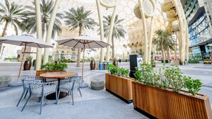 An outdoor seating area with round tables and chairs, surrounded by planters with greenery. - Cheval Maison Expo City Dubai (Dubai)