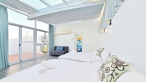 A hotel room with a large sliding glass door leading to an outdoor terrace, a bed with white linens, a sofa, and a painting on the wall. - Pescadores B&B (Magong)