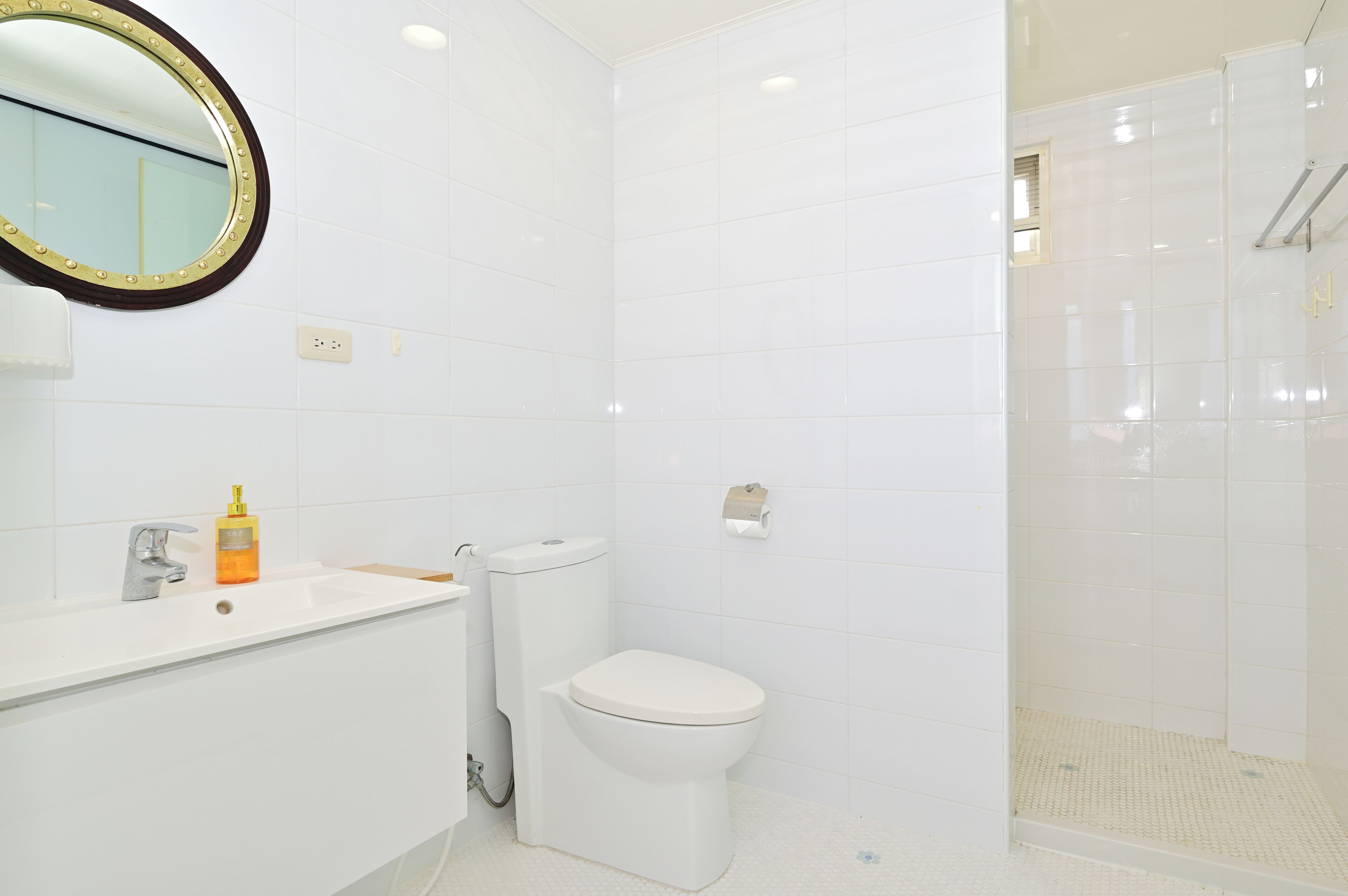 A bathroom with white tiles, a sink, a toilet, and a shower area.