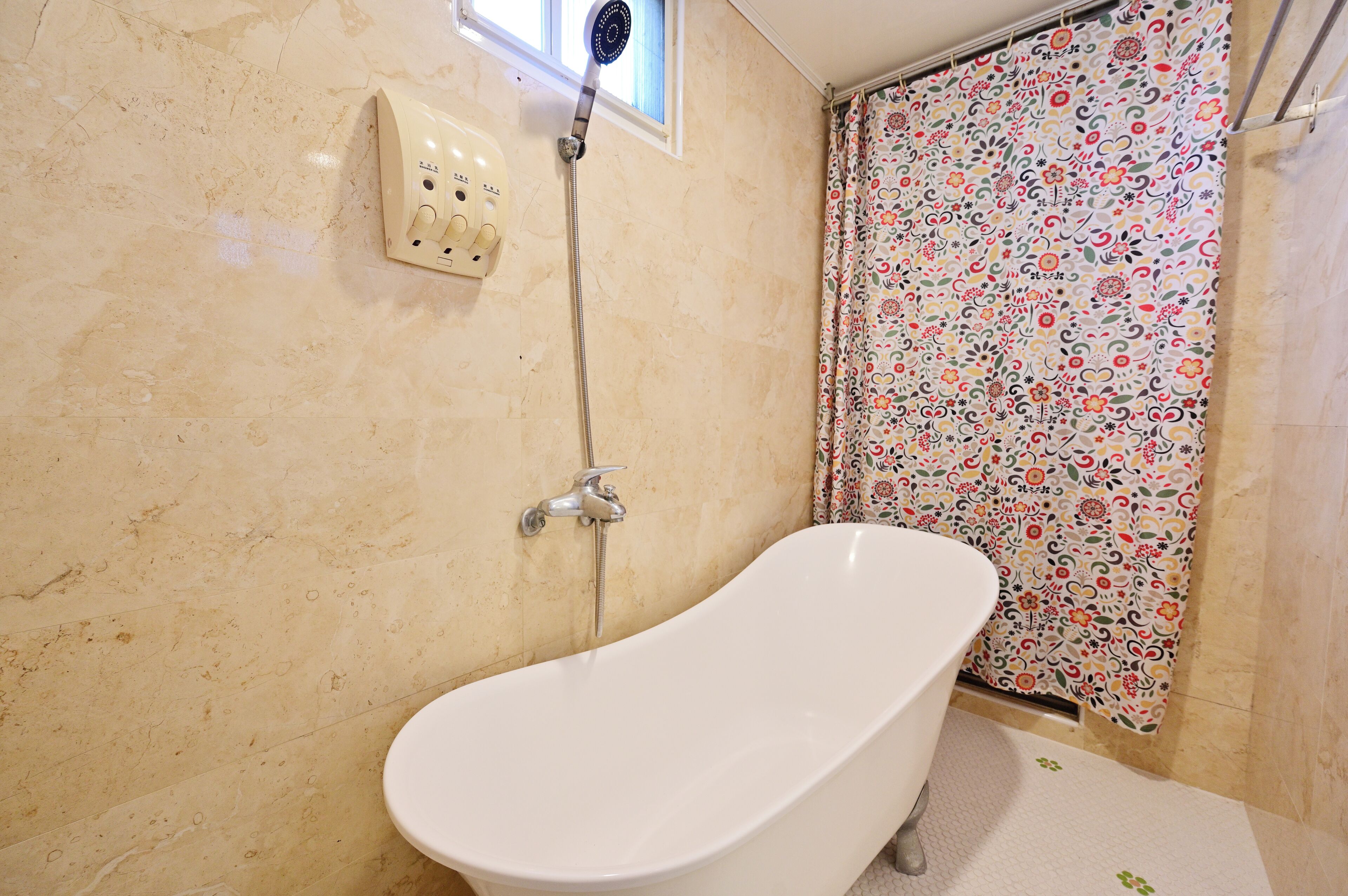 Un baño con una bañera independiente, un cabezal de ducha y una cortina de ducha con estampado floral.