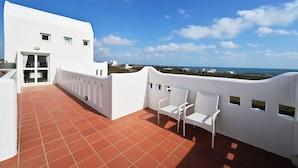 A white building with a terrace featuring red tiles, two white wicker chairs, and a view of the sea. - Pescadores B&B (Magong)