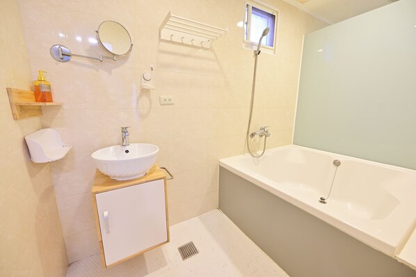 A modern bathroom with a white sink, a bathtub, a shower, a mirror, and a shelf with toiletries.