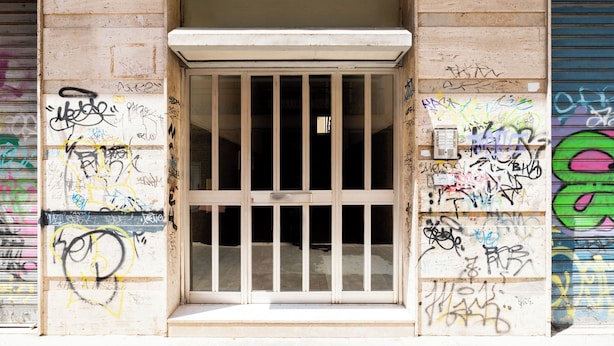 Entrada de un edificio con una puerta reja, rodeada de muros cubiertos de grafitis.