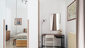 Un dormitorio con cama, mesita de noche, espejo, escritorio, silla y una obra de arte en la pared.