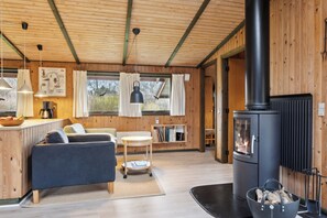 En mysig stuga med en soffa, ett litet bord, en bokhylla, en öppen spis och ett fönster med gardiner.