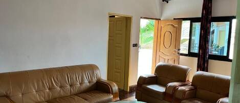 A living room with a brown leather sofa, a glass coffee table, and a wooden door.