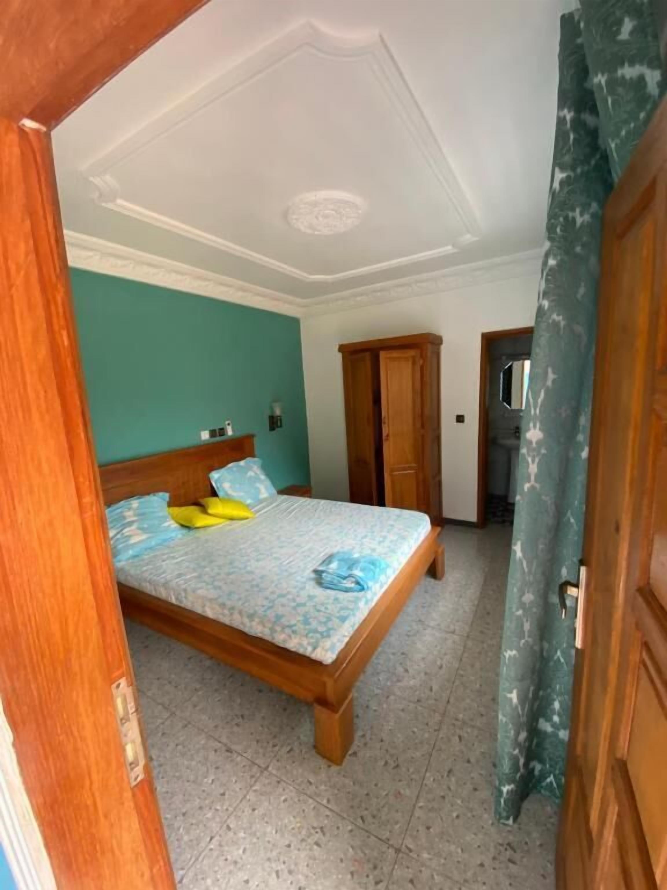 A bedroom with a wooden bed, teal walls, and a tiled floor.