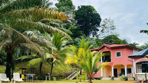 A pink house with a garden, palm trees, and a staircase leading to the entrance. - Prestige Beach Residence (Kribi)