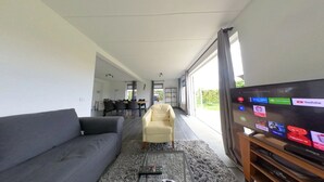A modern living room with a gray sofa, a beige armchair, and a flat-screen TV displaying various streaming services. - Topsleep Villa Lathum (Watervogel 12, 6988 CB LATHUM)