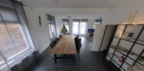A modern dining area with a long wooden table, black chairs, and a Christmas tree.