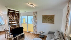 Un salon moderne avec un canapé d’angle gris, un téléviseur à écran plat posé sur un meuble en bois, une petite table d’appoint et une carte décorative accrochée au mur.