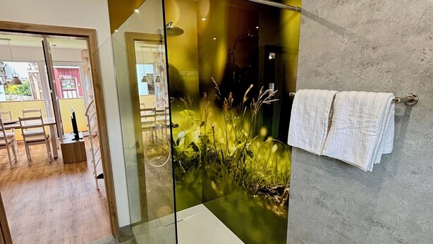 A modern bathroom with a glass shower enclosure, a towel rack, and a view of a dining area. - Comfortable, barrier-free vacation home in a quiet location with top facilities  (Kronach)