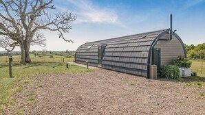 Een grote, gebogen kasconstructie met een metalen dak en een deur, omgeven door een grindpad en een grasveld.