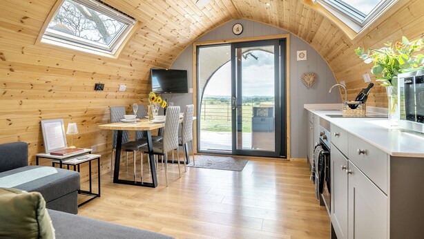 Een knus interieur van een chalet met een eethoek, keuken en een grote schuifpui naar een balkon.