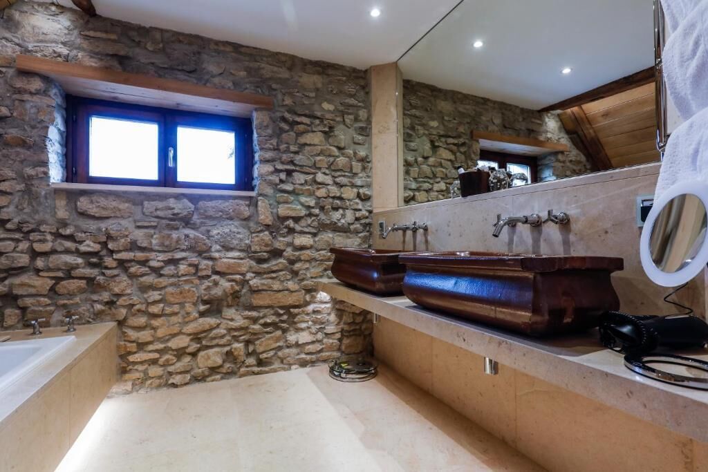 A bathroom with a stone wall, wooden vanity, and a bathtub.