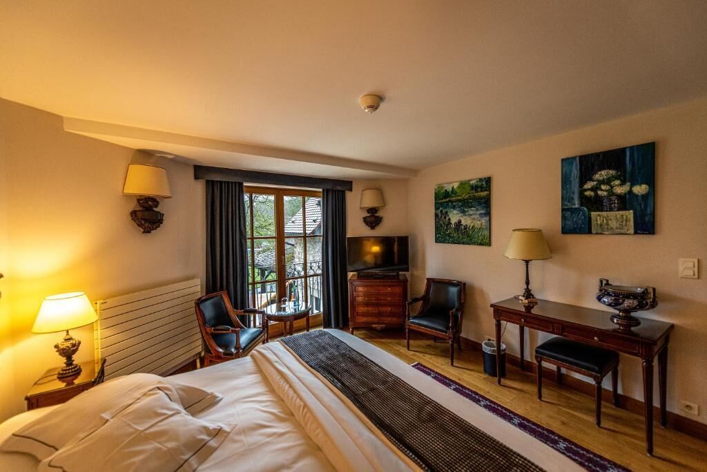 Una habitación de hotel con una cama, dos sillas, un escritorio, un televisor y obras de arte en las paredes.