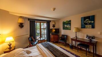 Una habitación de hotel con una cama, dos sillas, un escritorio, un televisor y obras de arte en las paredes.