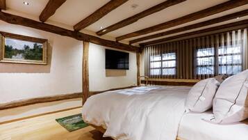 Een slaapkamer met zichtbare houten balken, een bed met witte beddengoed, een ingelijste foto aan de muur en een raam met jaloezieën.